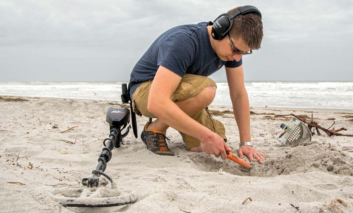 Detectorist recovering a beach target with a Garrett AT Max, Garrett pinpointer and sand scoop