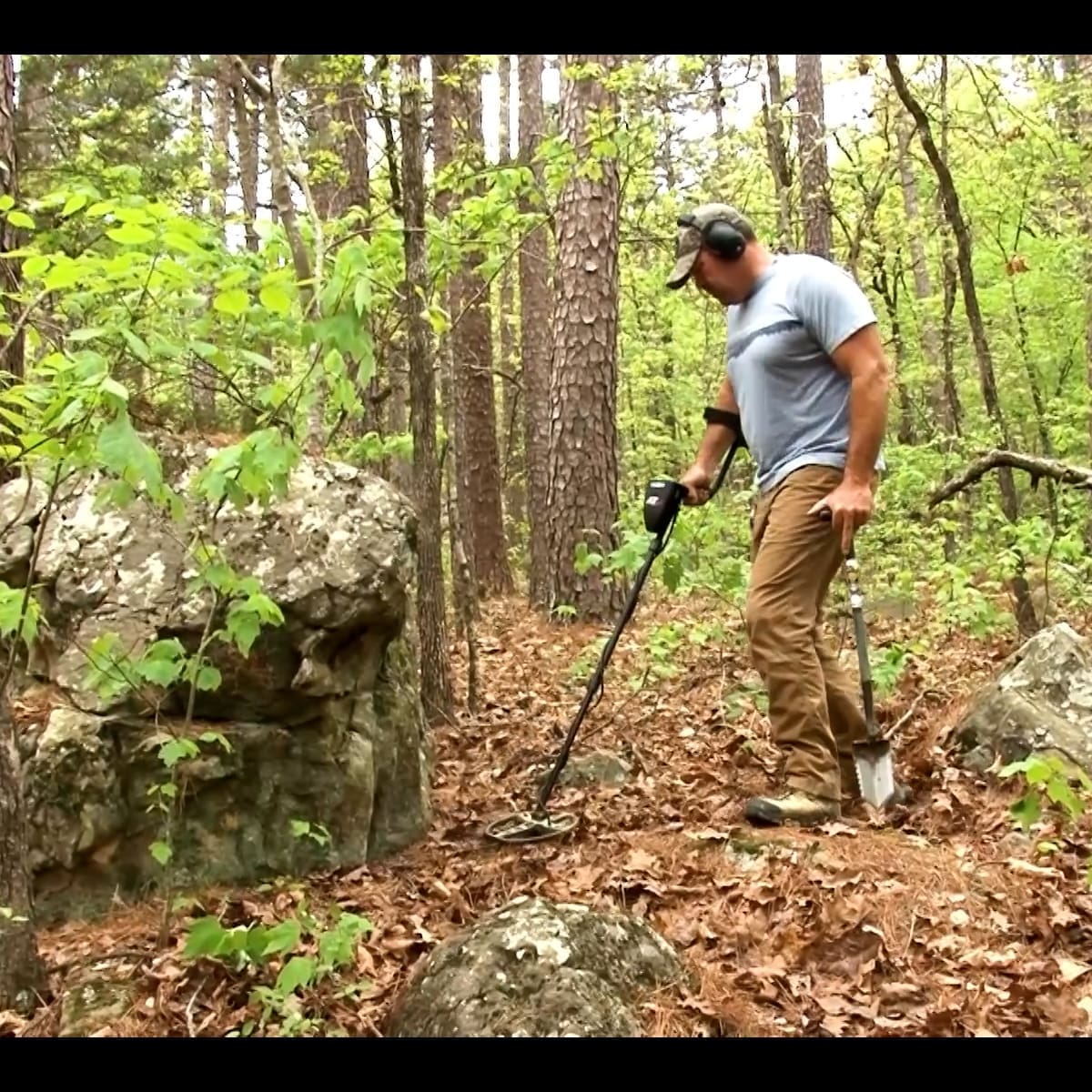 Detectorist swinging a Garrett AT Max metal detector through a wooded relic site with wireless headphones on