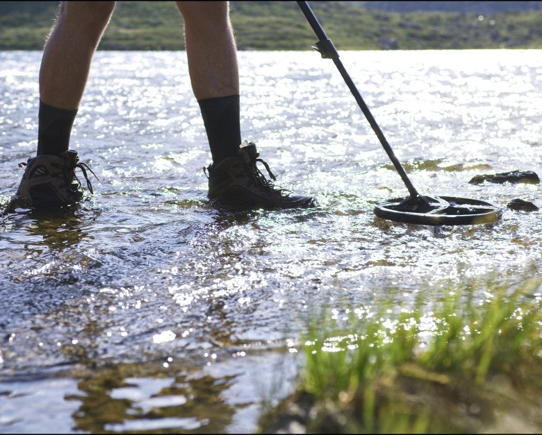 Detectorist wading a shallow lake swinging an XP Deus II with an FMF search coil